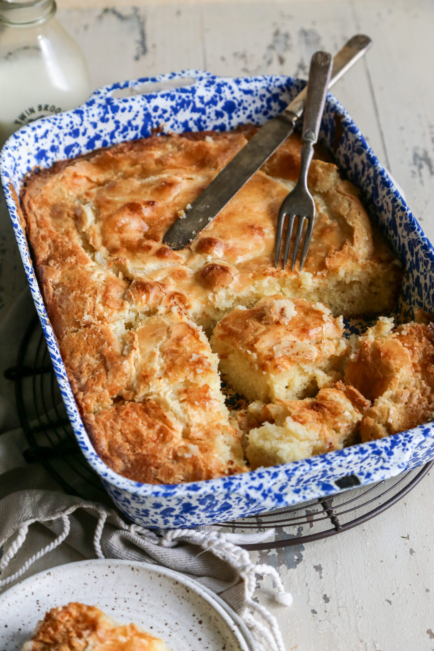 A Ooey Gooey Butter Cake from scratch in a blue and white baking dish with rustic knife on top. 