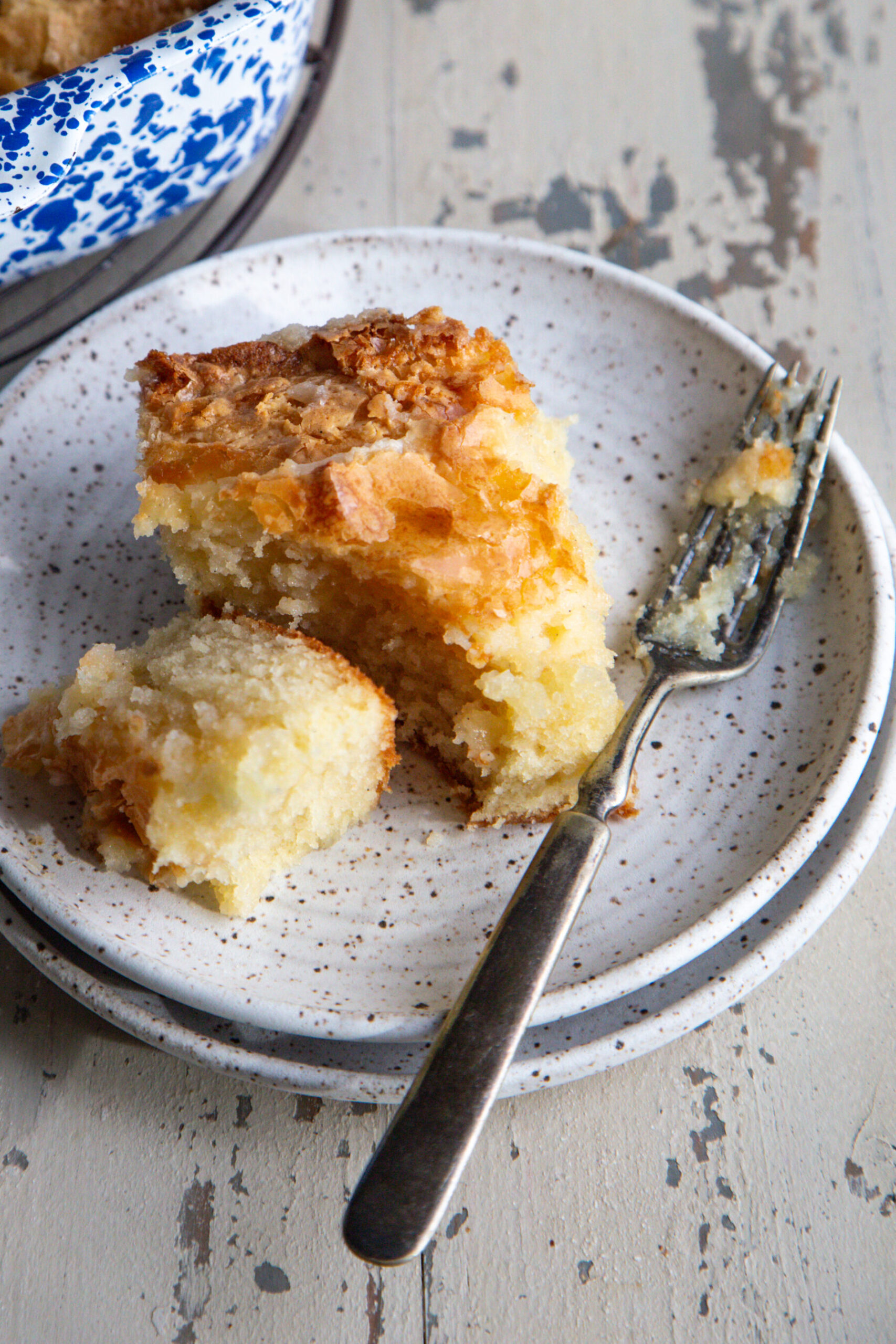 A slice of ooey gooey butter cake on a speckled plate with a fork on the side. 