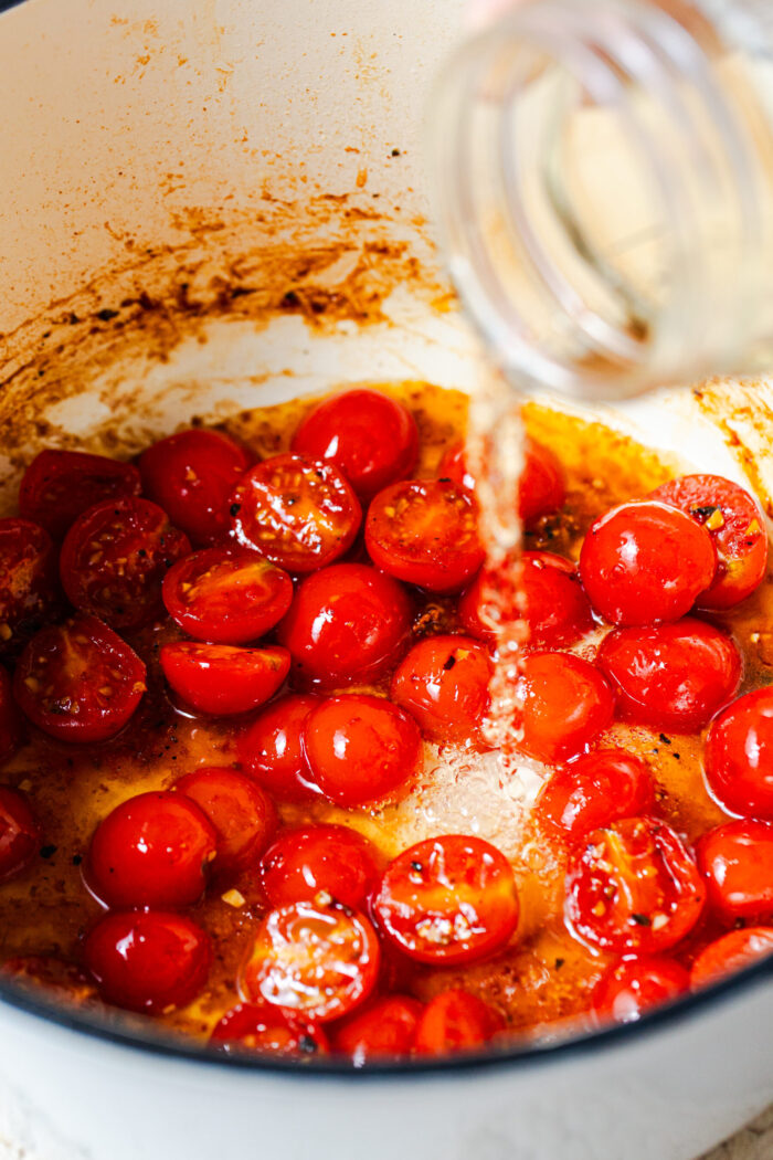 Deglazing a pan with tomatoes and white wine for one pot chicken florentine pasta