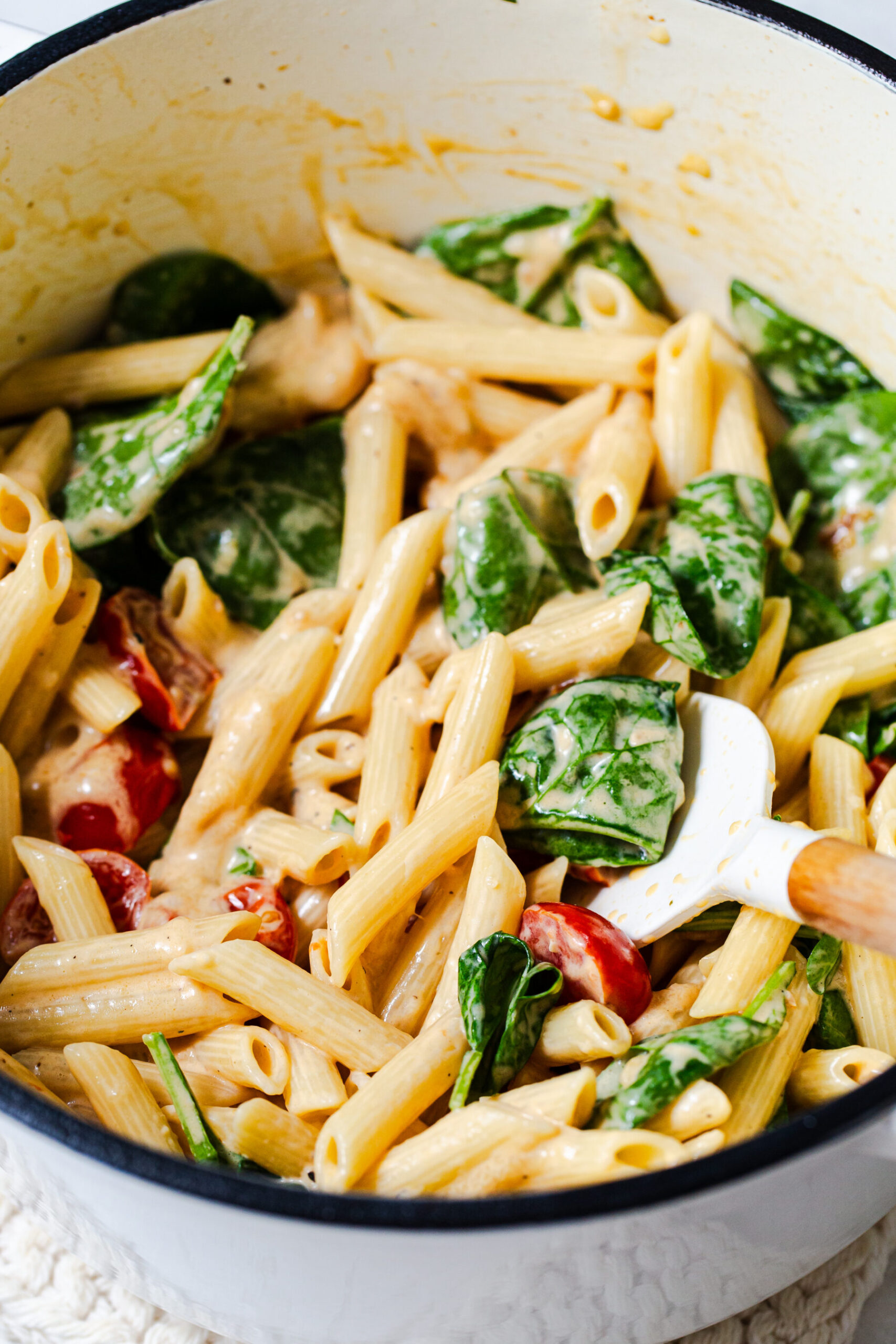Stirring together spinach, tomatoes and pasta for one pot chicken florentine pasta in a close up photo