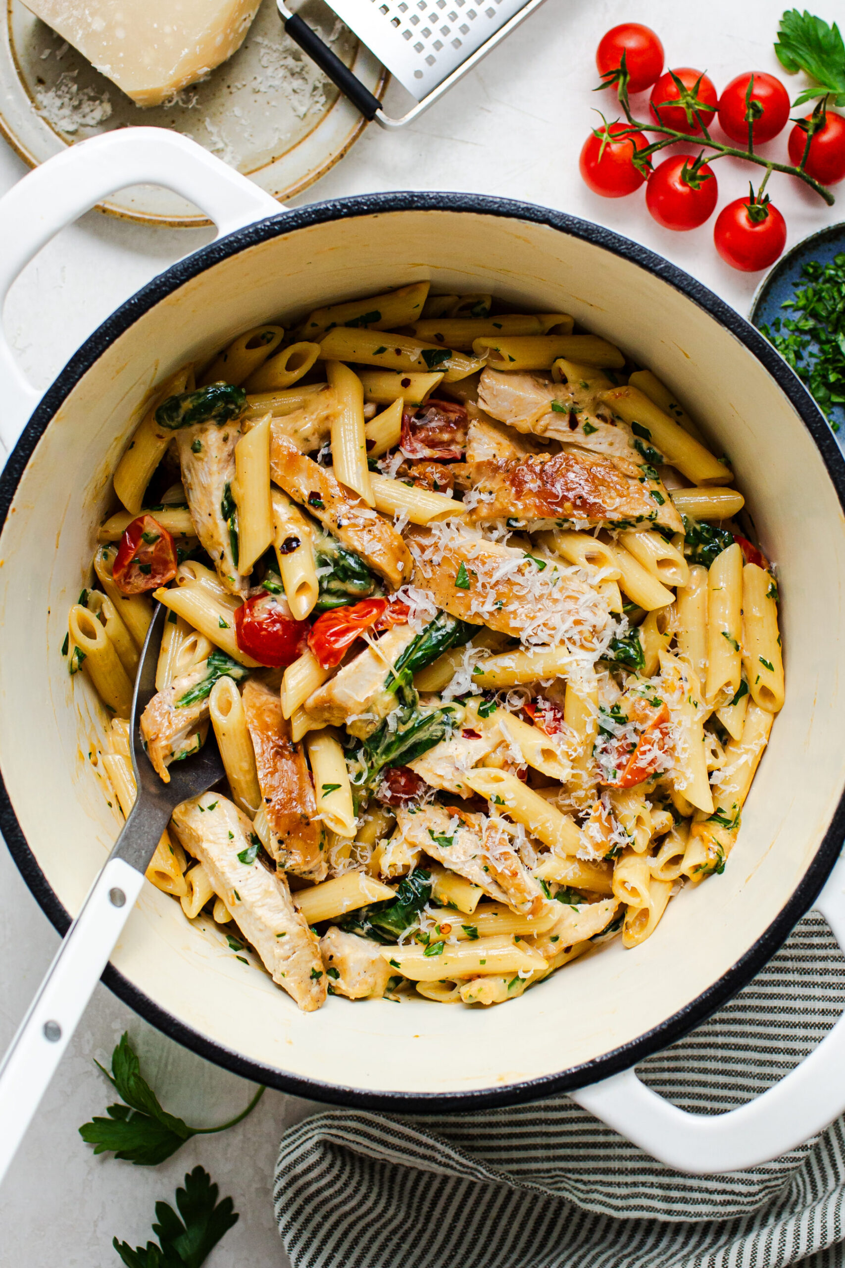 Overhead photo in cast iron pan of one pot chicken Florentine pasta with fresh parmesan on top and surrounded with tomatoes, red pepper flakes and parmesan. 