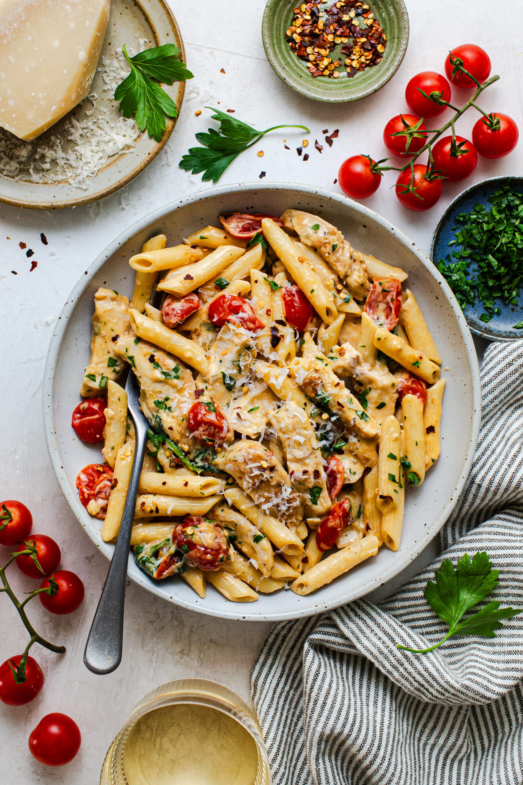 Overhead photo of large bowl of one pot chicken Florentine pasta with a spoon in the pasta for serving, and surrounded by the ingredients.
