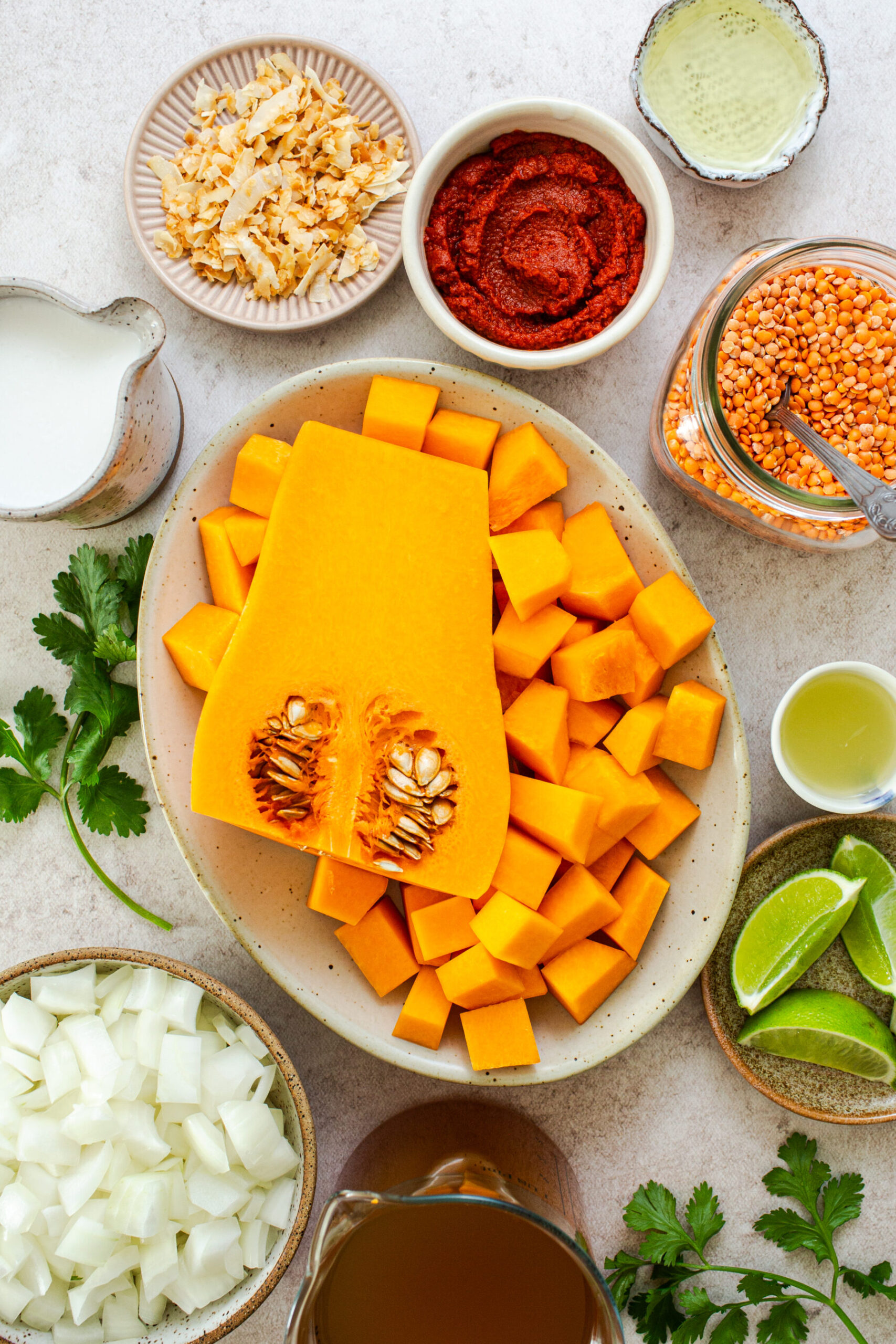 Overhead photo of butternut squash soup ingredients shot from overhead including cubes of butternut squash, onion, lime wedges, vegetable stock and cilantro leaves. 