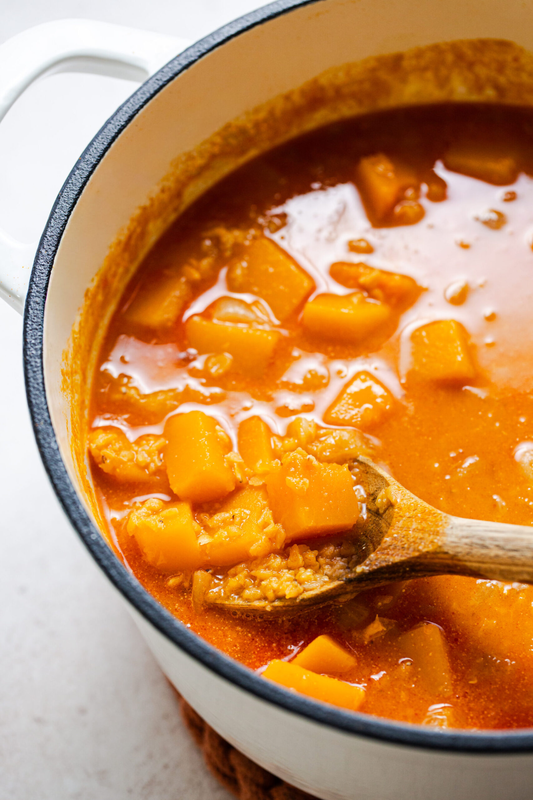Butternut squash soup ingredients on a wooden spoon in a Dutch Oven to show the texture. 